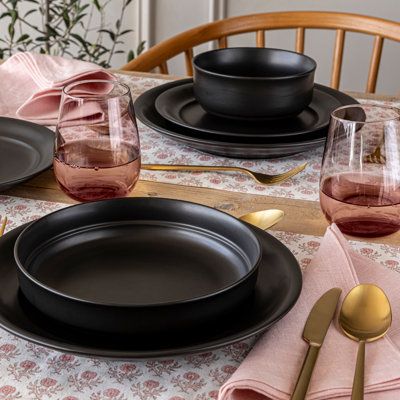 the table is set with black plates and pink napkins