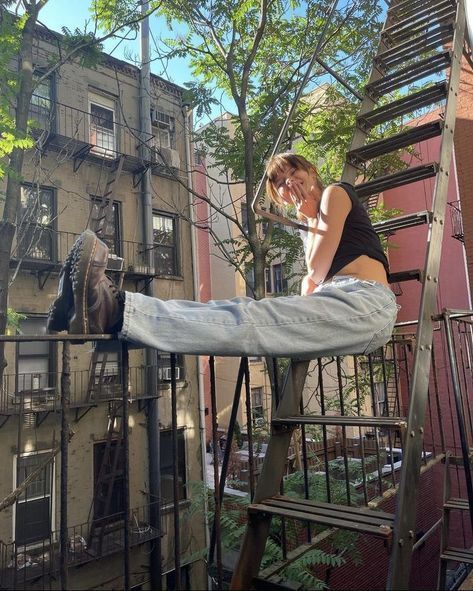 a woman sitting on top of a metal railing next to a building and talking on a cell phone