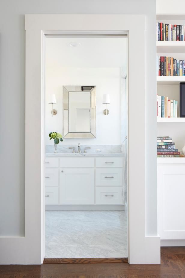 an open door leading to a bathroom with white cabinets and bookcases on the wall