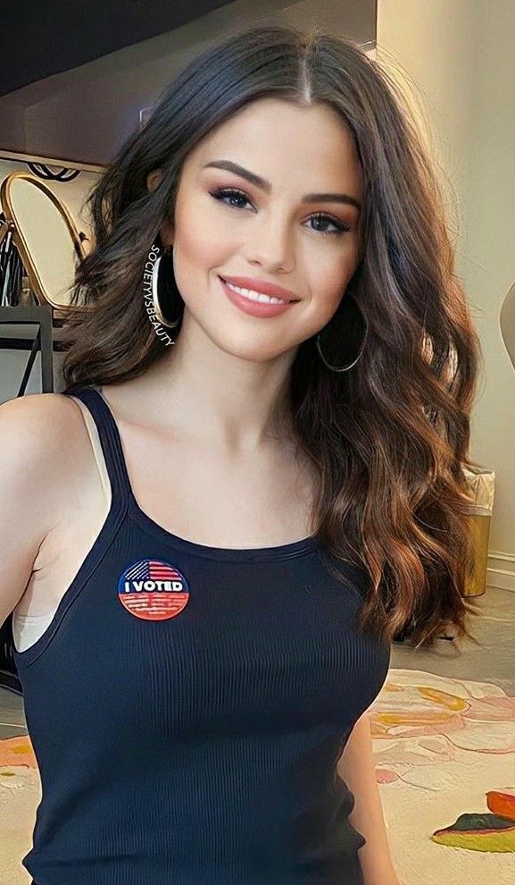 a beautiful young woman standing in front of a mirror wearing a black tank top and silver hoop earrings