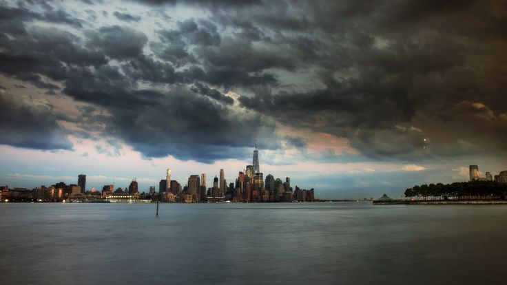 a city skyline is shown under dark clouds over the water in front of a large body of water