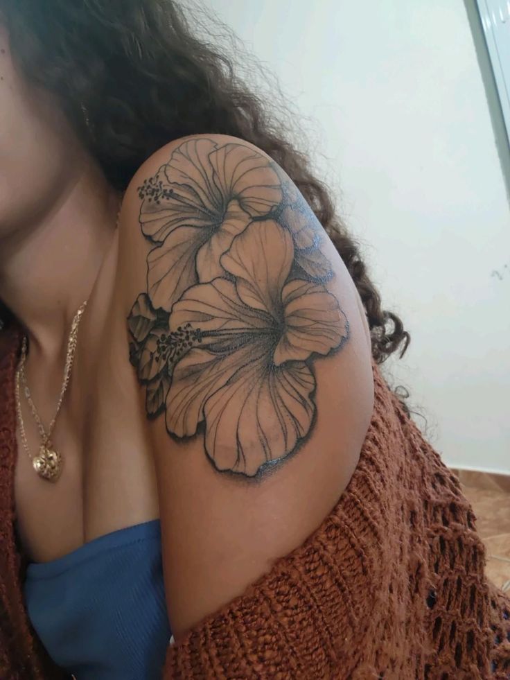 a woman's arm with a flower tattoo on the left side of her shoulder