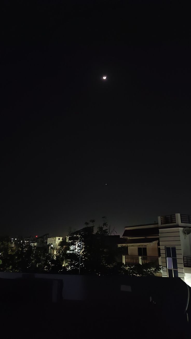 the moon is shining in the dark sky above some buildings and trees at night time