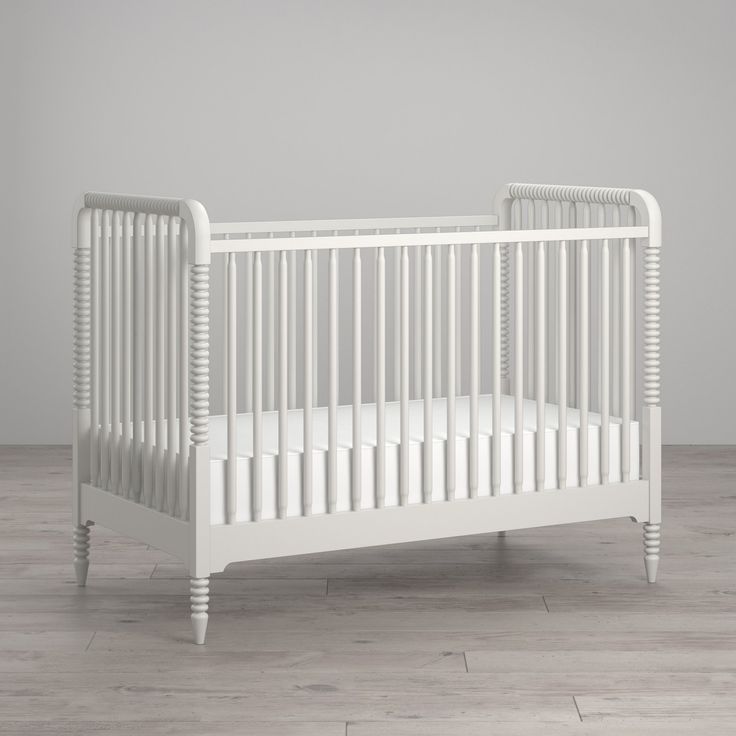 an empty white crib on a wooden floor