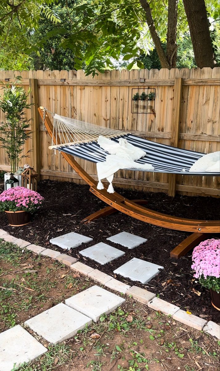 a hammock is in the middle of a garden with pink flowers around it