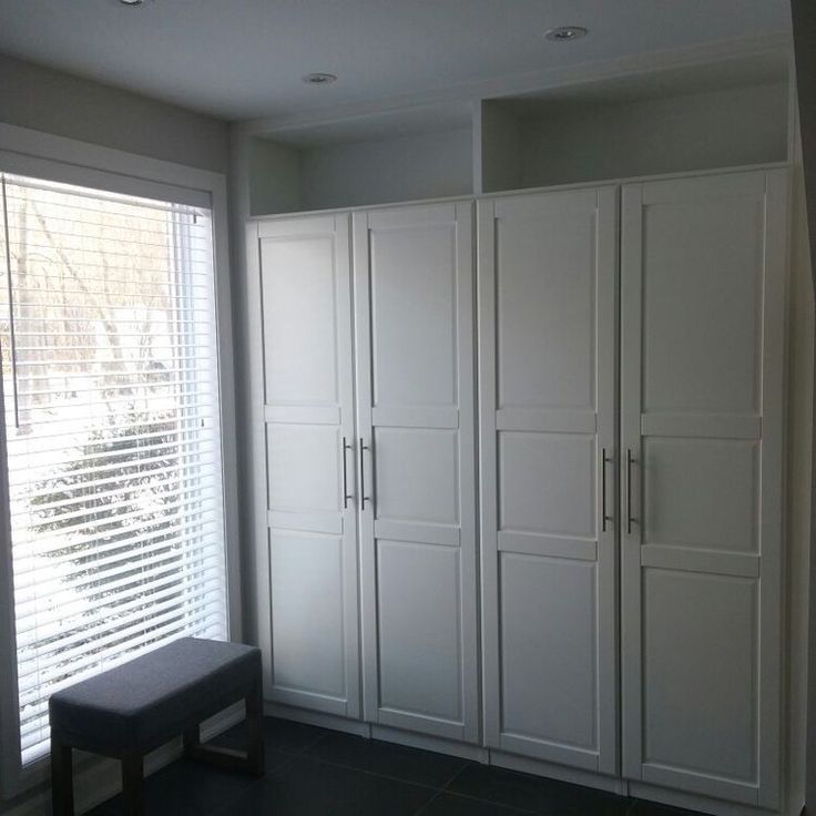 an empty room with white cupboards and a bench in front of the window,