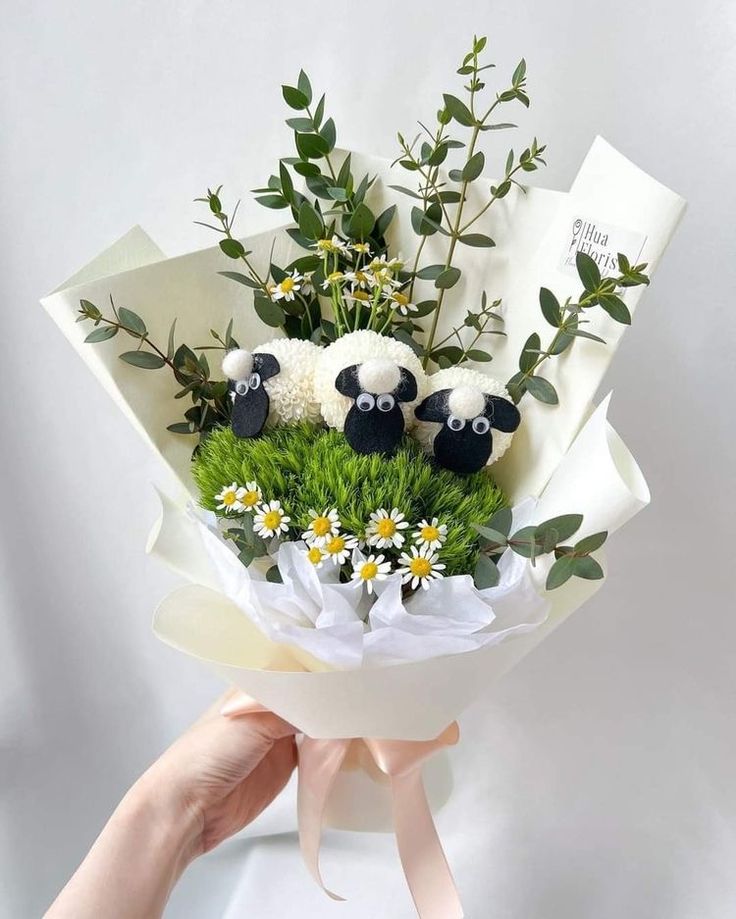 someone is holding a bouquet with fake sheep in the middle and daisies on the bottom