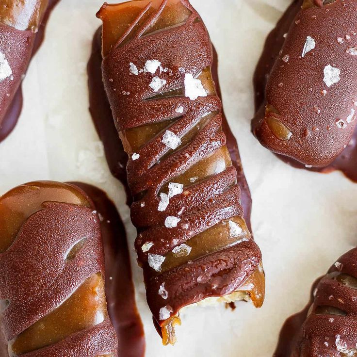 chocolate covered donuts with white sprinkles on them sitting on wax paper