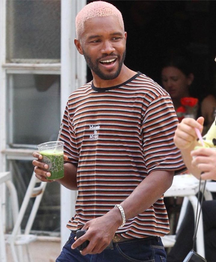 a man with pink hair is holding a green smoothie and smiling at the camera