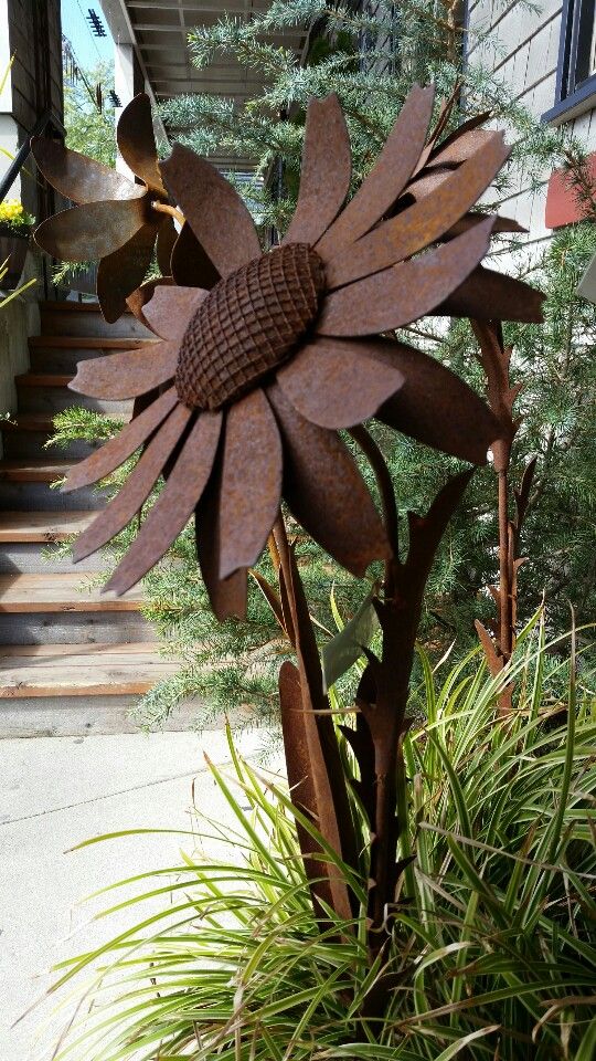 a large metal flower sitting on top of a planter next to a staircase leading up to a house