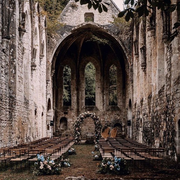 an old church with rows of chairs and flowers on the aisle, surrounded by stone walls