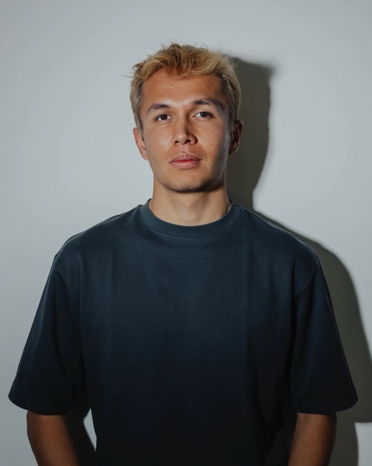 a young man standing in front of a white wall wearing a black t - shirt