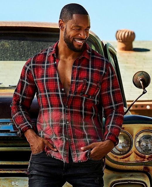 a man standing in front of an old truck with his hands in his pockets and smiling