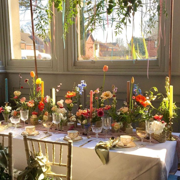 a table with flowers and candles is set up in front of a window for a party