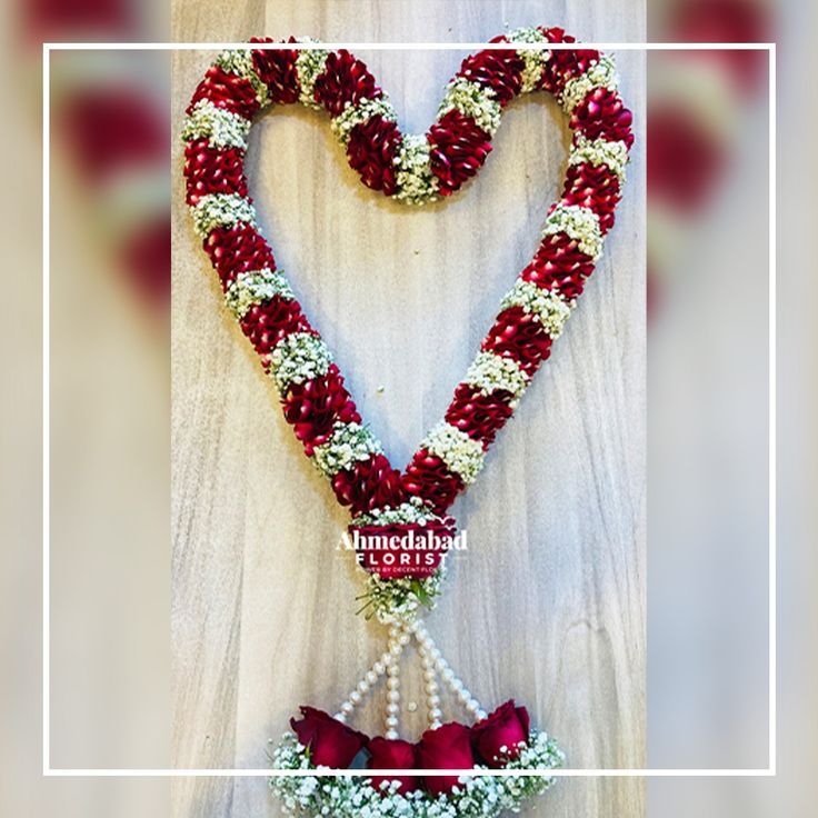 a heart - shaped decoration with flowers and pearls hanging from it's sides in front of a white frame