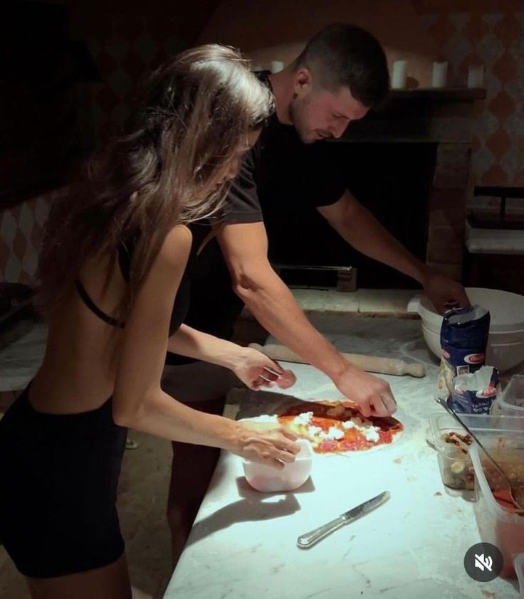 a man and woman are preparing pizzas on a counter top in the kitchen at night