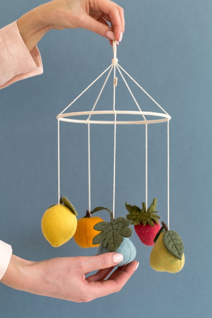 a hand holding a mobile with fruit hanging from it's sides and two hands reaching for one