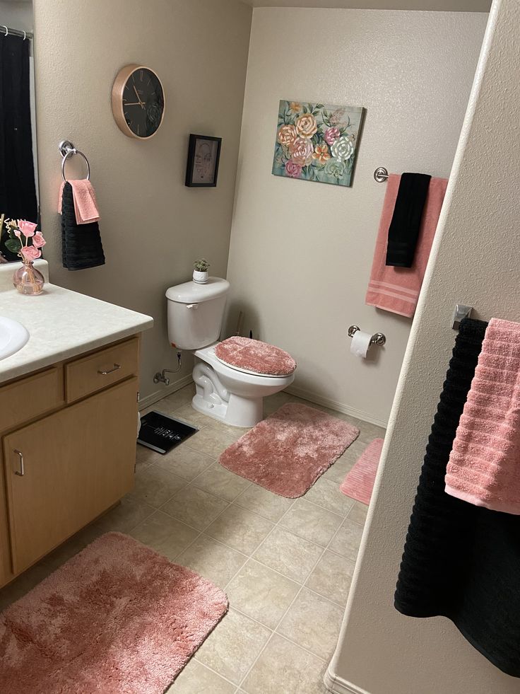 a bathroom with pink rugs on the floor and black towels hanging above the toilet