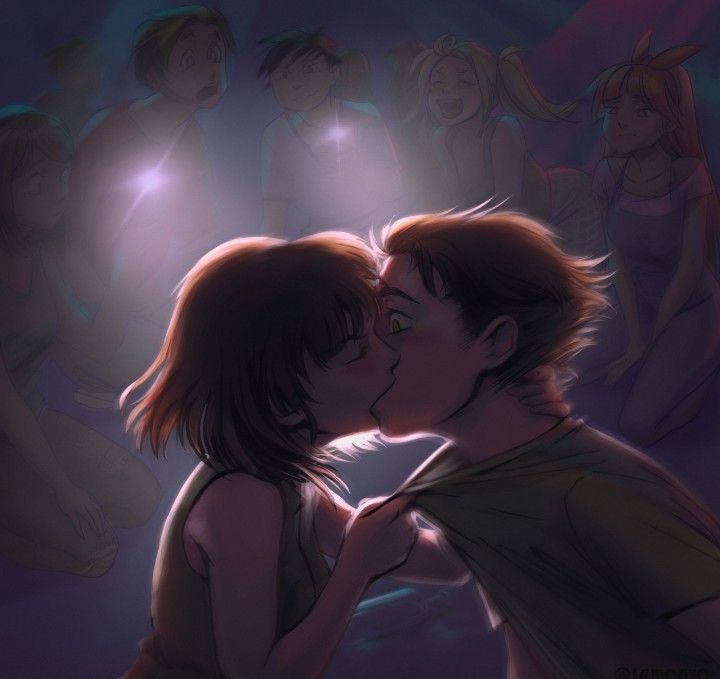 two people kissing in front of a group of other people with lights shining on them