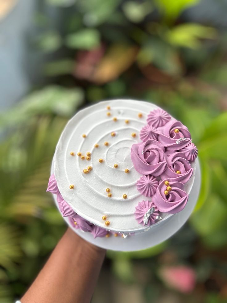 a hand holding a cake with pink flowers on it and gold sprinkles