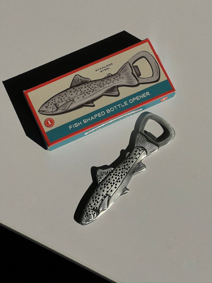 a fish shaped bottle opener sitting on top of a white table next to a box