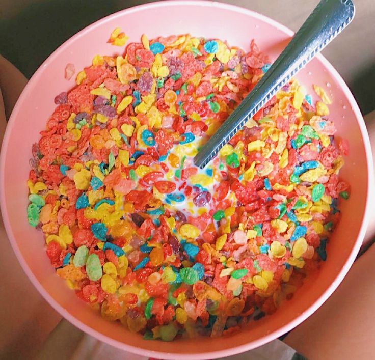 a pink bowl filled with lots of cereal and sprinkles next to a person's hand