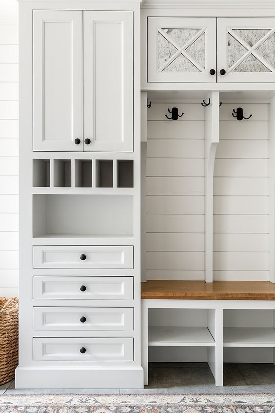 a room with white cabinets and drawers next to a wall mounted coat rack in the corner