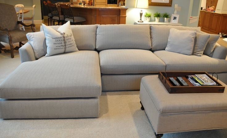 a living room with a sectional couch and footstool on the floor in front of a coffee table