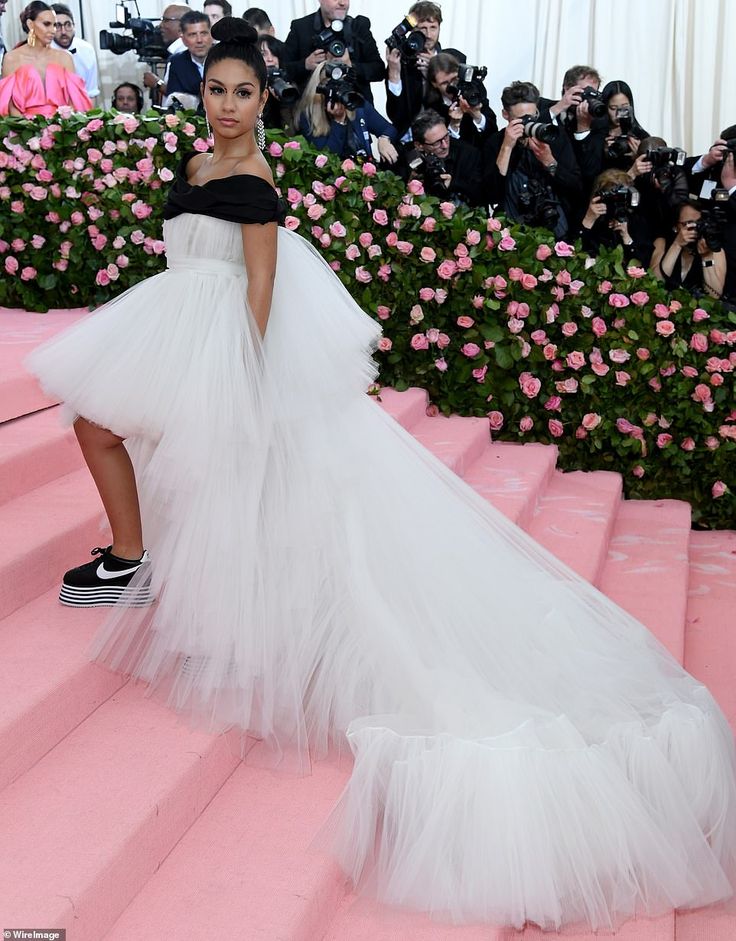 a woman in a white dress is standing on some steps with pink flowers behind her