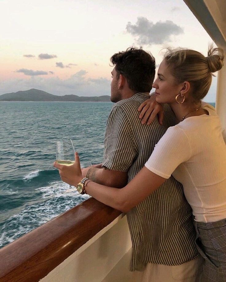 a man and woman on a boat looking out at the ocean while holding wine glasses