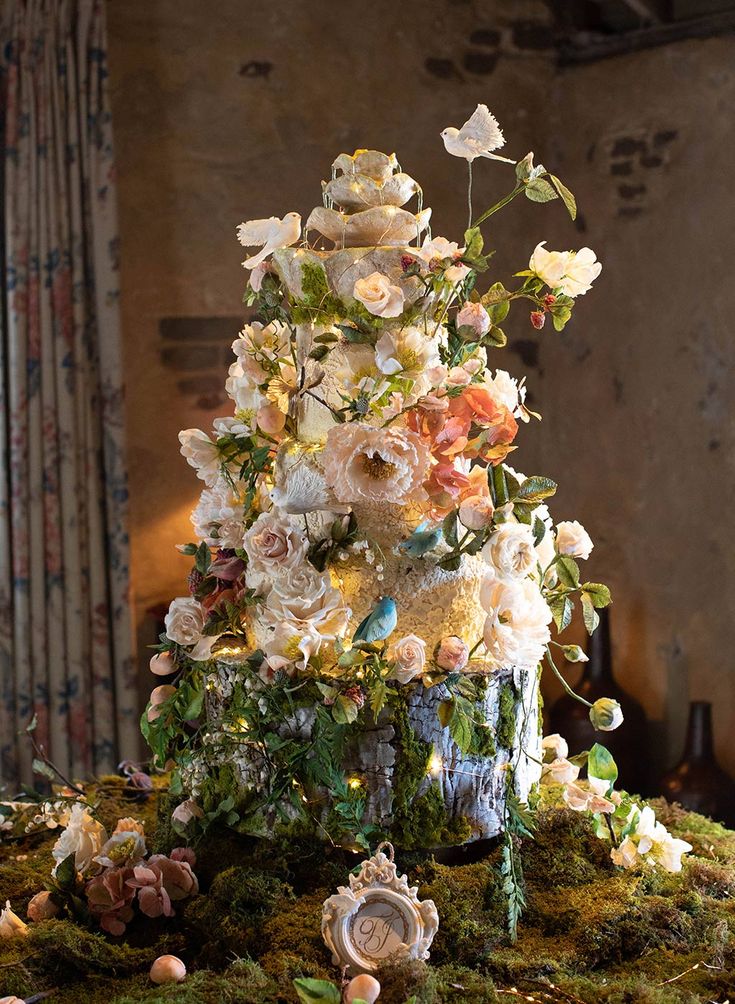 an elaborately decorated christmas tree in the middle of a moss covered table with flowers on it