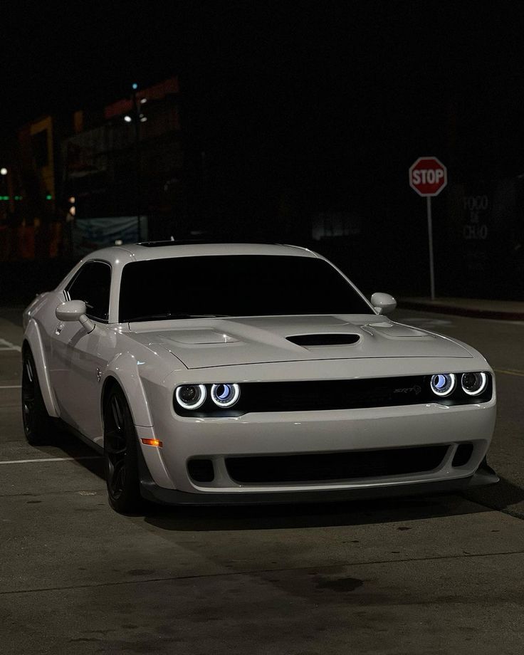 a white sports car parked on the side of the road at night with its lights on