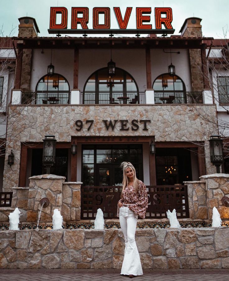 a woman standing in front of a stone building with a sign above it that reads denver 977 west