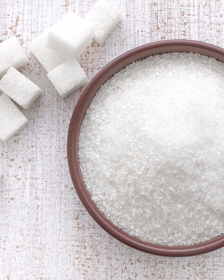 a bowl filled with sugar next to cubes of sugar on top of a table