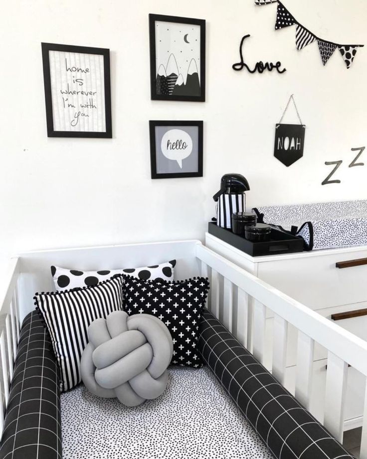 a white crib with black and white decor on the wall above it is filled with pillows