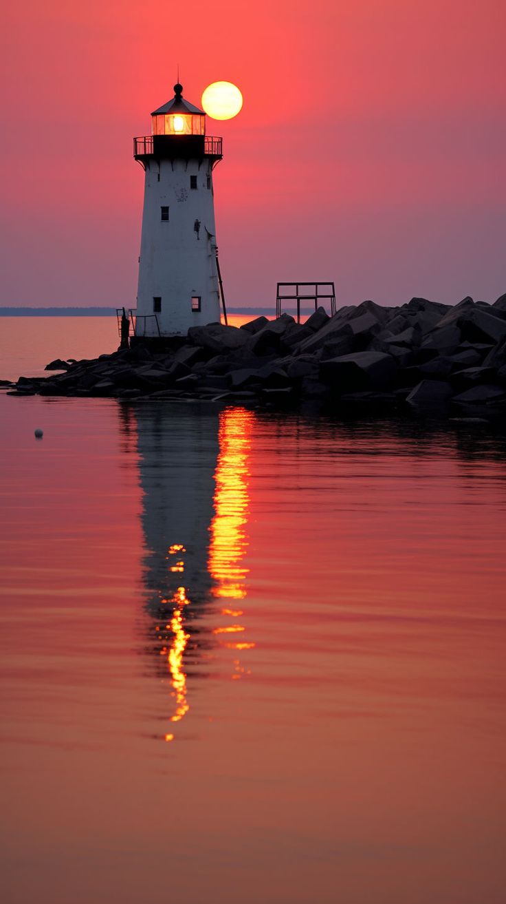 a light house sitting on top of a body of water next to the ocean at sunset