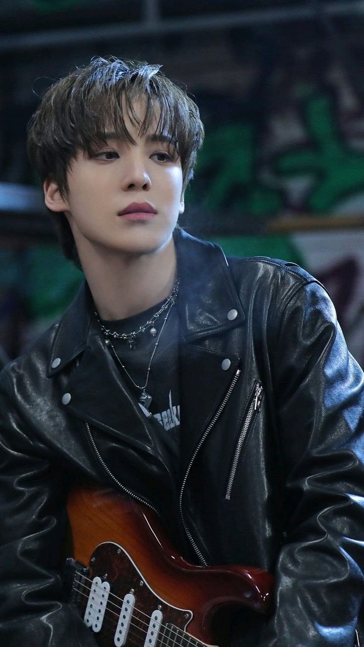 the young man is playing an electric guitar in front of graffiti covered walls and wearing a black leather jacket