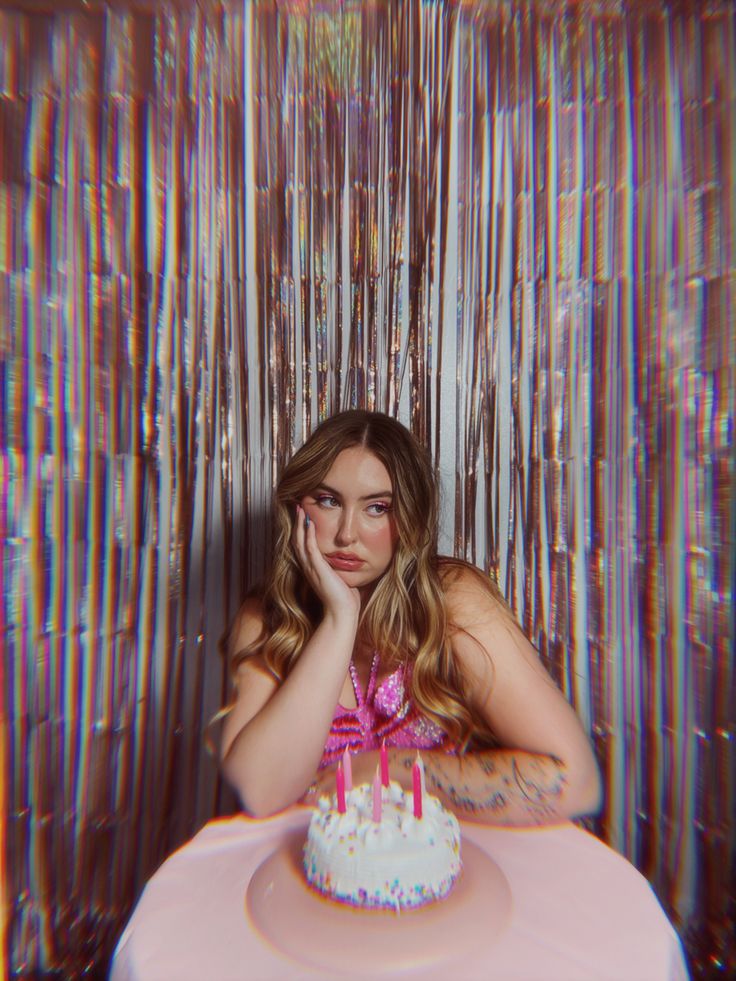 a woman sitting at a table with a cake in front of her and colorful curtains behind her