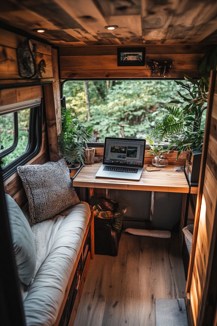 a laptop computer sitting on top of a wooden desk next to a window filled with plants