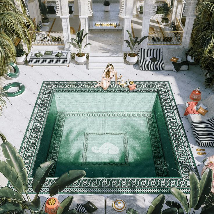 a woman sitting on the edge of a swimming pool surrounded by palm trees and potted plants