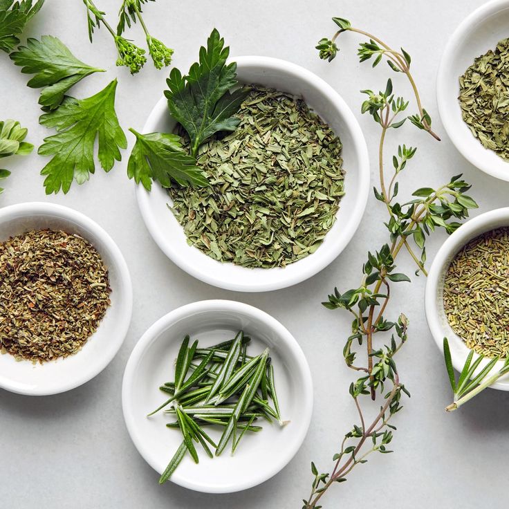 four white bowls filled with herbs on top of a table