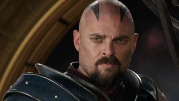 a bald man in armor looks at the camera with an evil look on his face