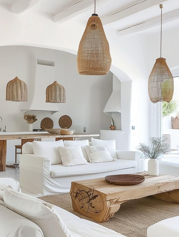 a living room filled with white furniture and hanging lights over the couches in front of a kitchen