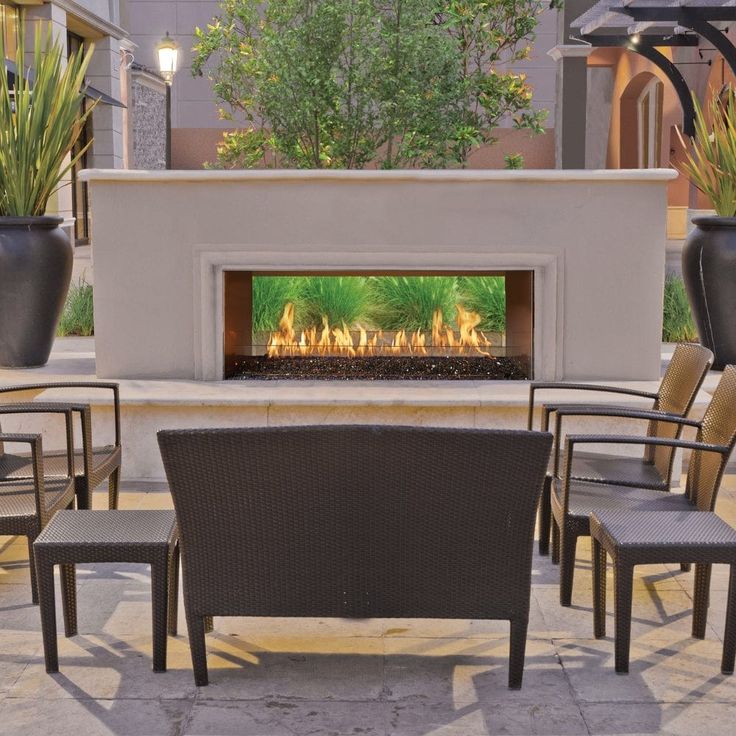 an outdoor fireplace with chairs around it and plants on the outside patio area in front of it