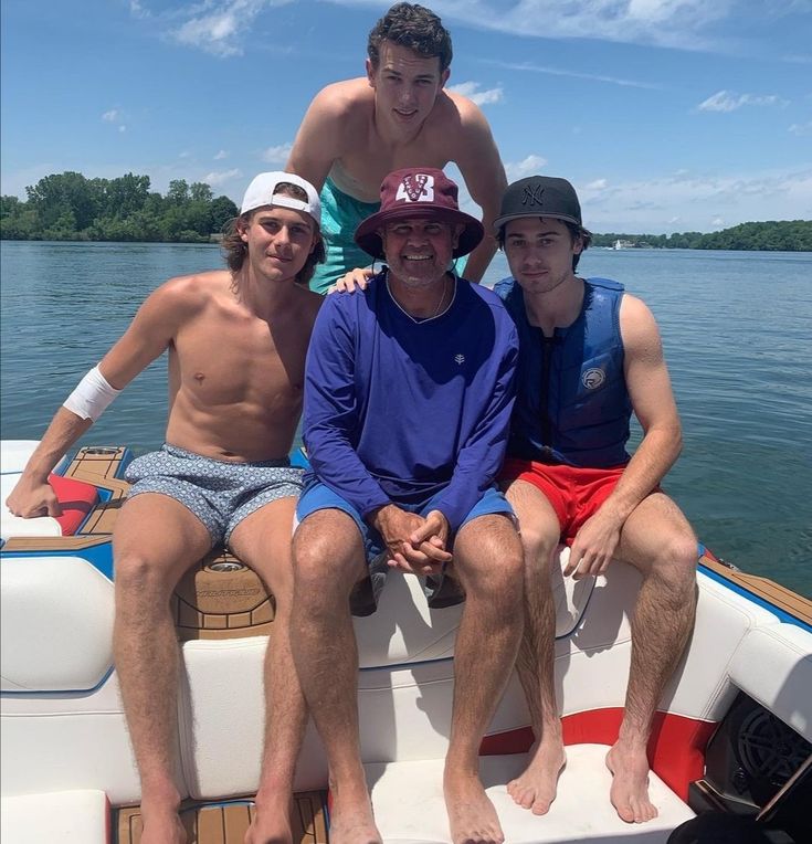 three men are sitting on the back of a boat in the water with one man wearing a hat