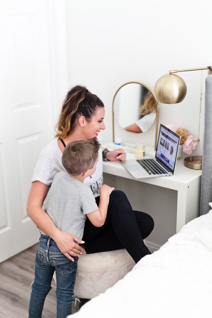 a woman sitting on a stool with a child using a laptop computer in front of her