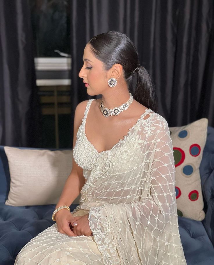 a woman sitting on top of a blue couch wearing a white sari and jewelry