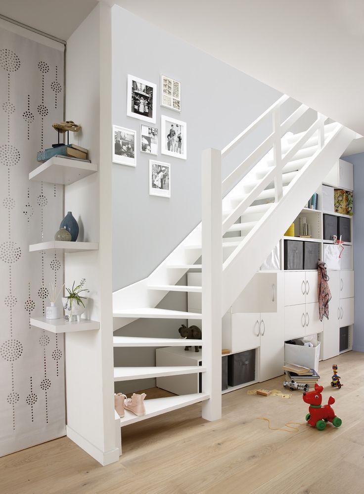 there is a white staircase in the living room with toys on the floor and shelves