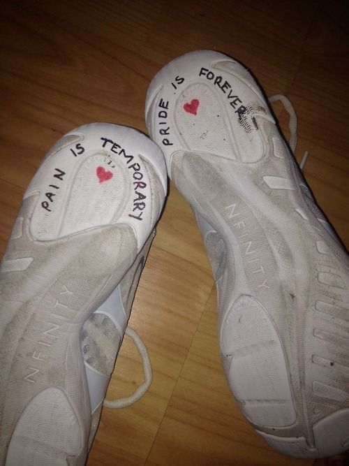 two pairs of white shoes with writing on them sitting on top of a wooden floor