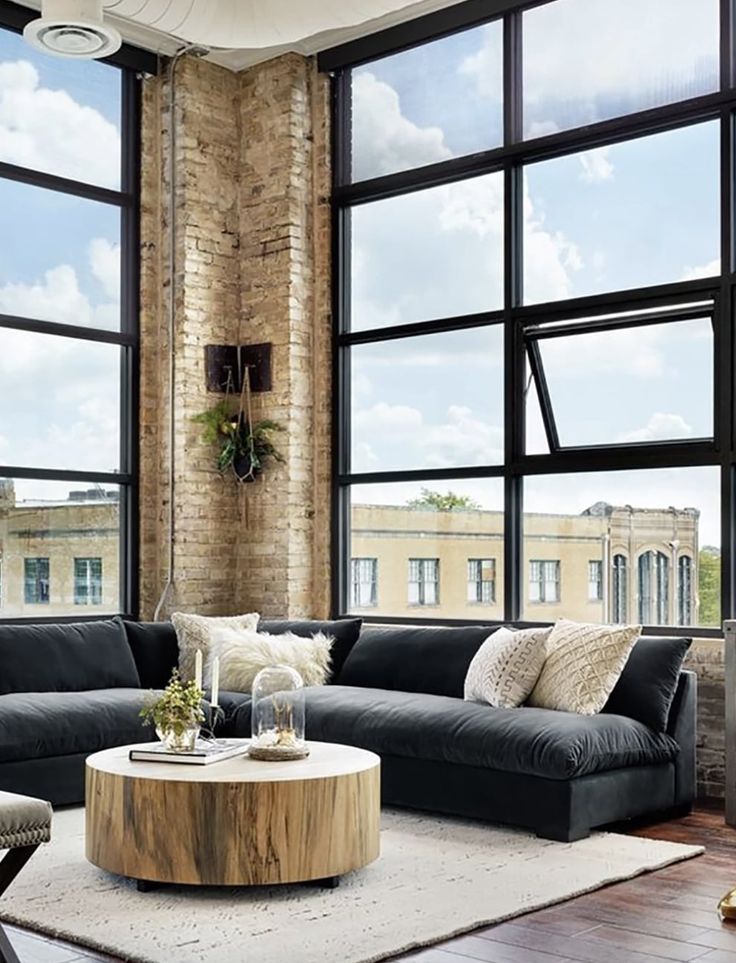 a living room filled with furniture next to large windows and a tall brick building in the background